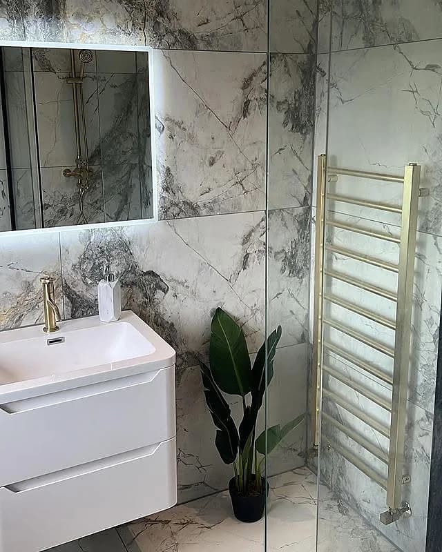 Marble-tiled bathroom with walk-in shower and gold heated towel rail, completed in Leeds by CLM Projects