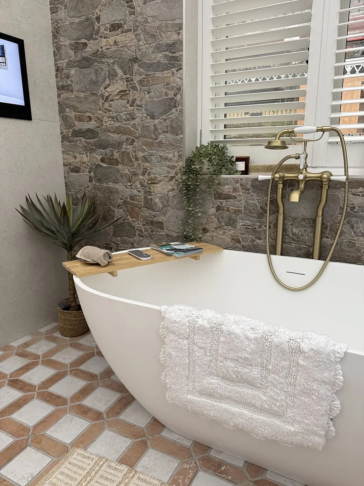 Freestanding bath against a natural stone feature wall with brass telephone taps, completed in Leeds by CLM Projects